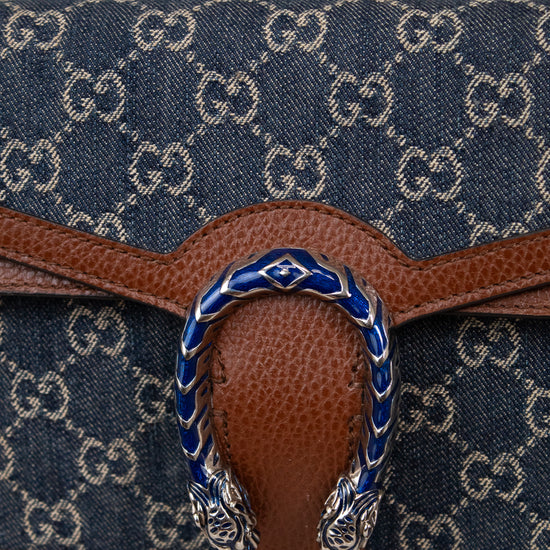 Close-up of a denim handbag with brown leather details and blue and silver buckle on a white background