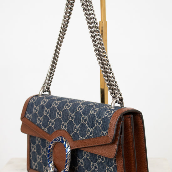 Designer handbag with blue pattern and brown leather accents on a white background
