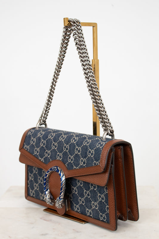 Designer handbag with blue pattern and brown leather accents on a white background