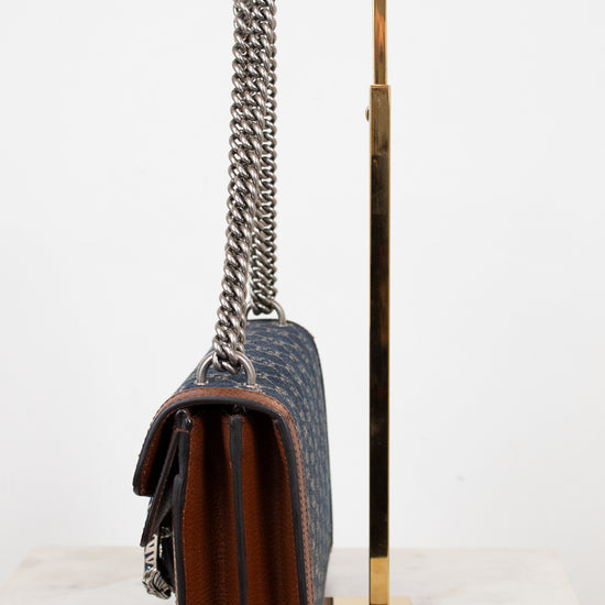 Designer handbag with chain detail on a stand against a white background