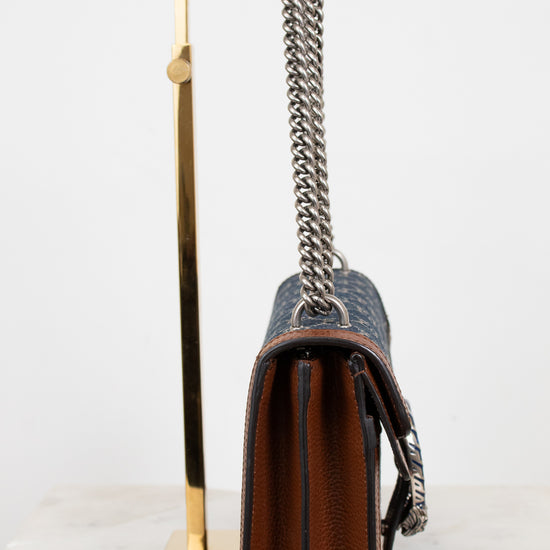 Designer handbag with silver chain strap on a stand against a white background
