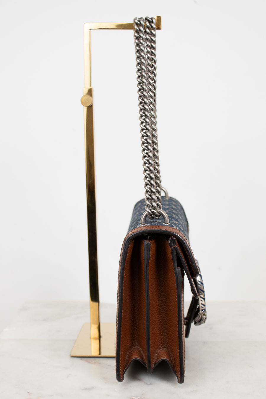 Designer handbag with silver chain strap on a stand against a white background