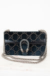 A dark teal velvet shoulder bag with a gold-tone GG monogram pattern, a silver chain strap and a silver-tone chain strap with a rhinestone-embellished Gucci dionysus clasp, shown on a white marble surface against a white background.