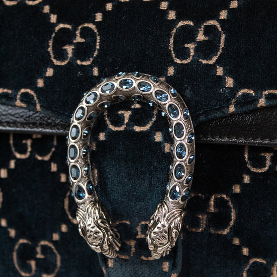Close-up of a Gucci shoulder bag with  black leather with the signature GG monogram in beige, featuring the iconic dionysus clasp with blue rhinestones and silver-tone snake heads.