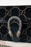 Close-up of a Gucci shoulder bag with  black leather with the signature GG monogram in beige, featuring the iconic dionysus clasp with blue rhinestones and silver-tone snake heads.