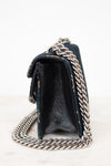 A close-up side view of a black leather handbag with a chunky silver chain strap, resting on a light marble surface against a white background.