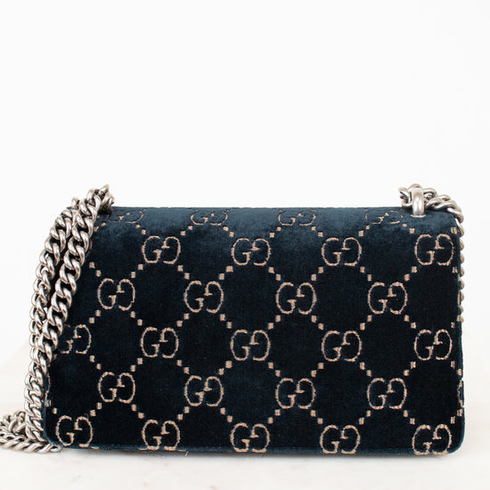 A dark teal blue velvet Gucci shoulder bag with the signature GG monogram pattern in beige, featuring a silver-tone chain strap.