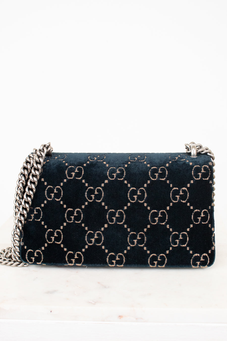 A dark teal blue velvet Gucci shoulder bag with the signature GG monogram pattern in beige, featuring a silver-tone chain strap.