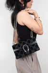 A woman wearing a black tank top and beige pants carries a teal Gucci shoulder bag with the brand's signature GG monogram pattern and a silver-tone dionysus clasp, shown from a side-back angle against a plain light gray background.