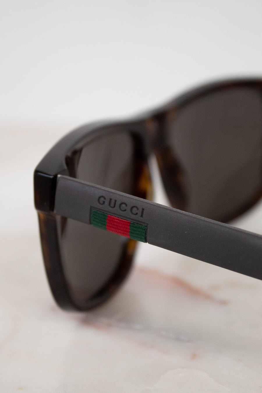 Close-up of Gucci sunglasses with dark brown tortoiseshell frames, dark lenses, and the signature green and red web stripe detail on the temple arm.
