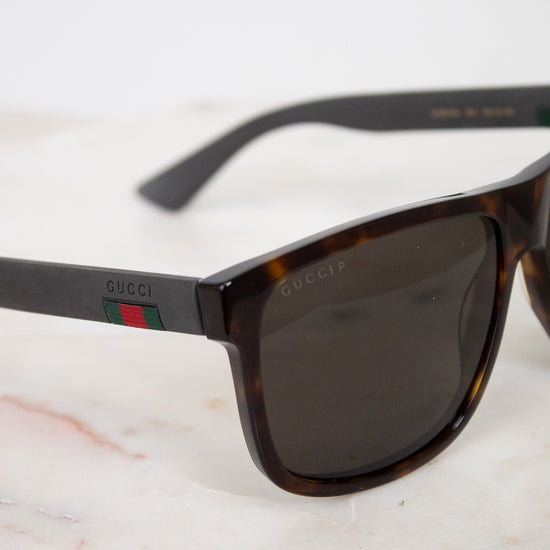 Gucci sunglasses with a dark tortoiseshell frame, dark lenses, and black temples featuring the signature green and red web stripe.