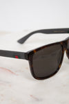 Gucci sunglasses with a dark tortoiseshell frame, dark lenses, and black temples featuring the signature green and red web stripe.
