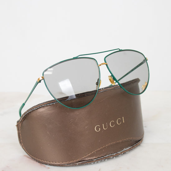 Teal aviator style glasses with gray lenses on a 'Gucci' case