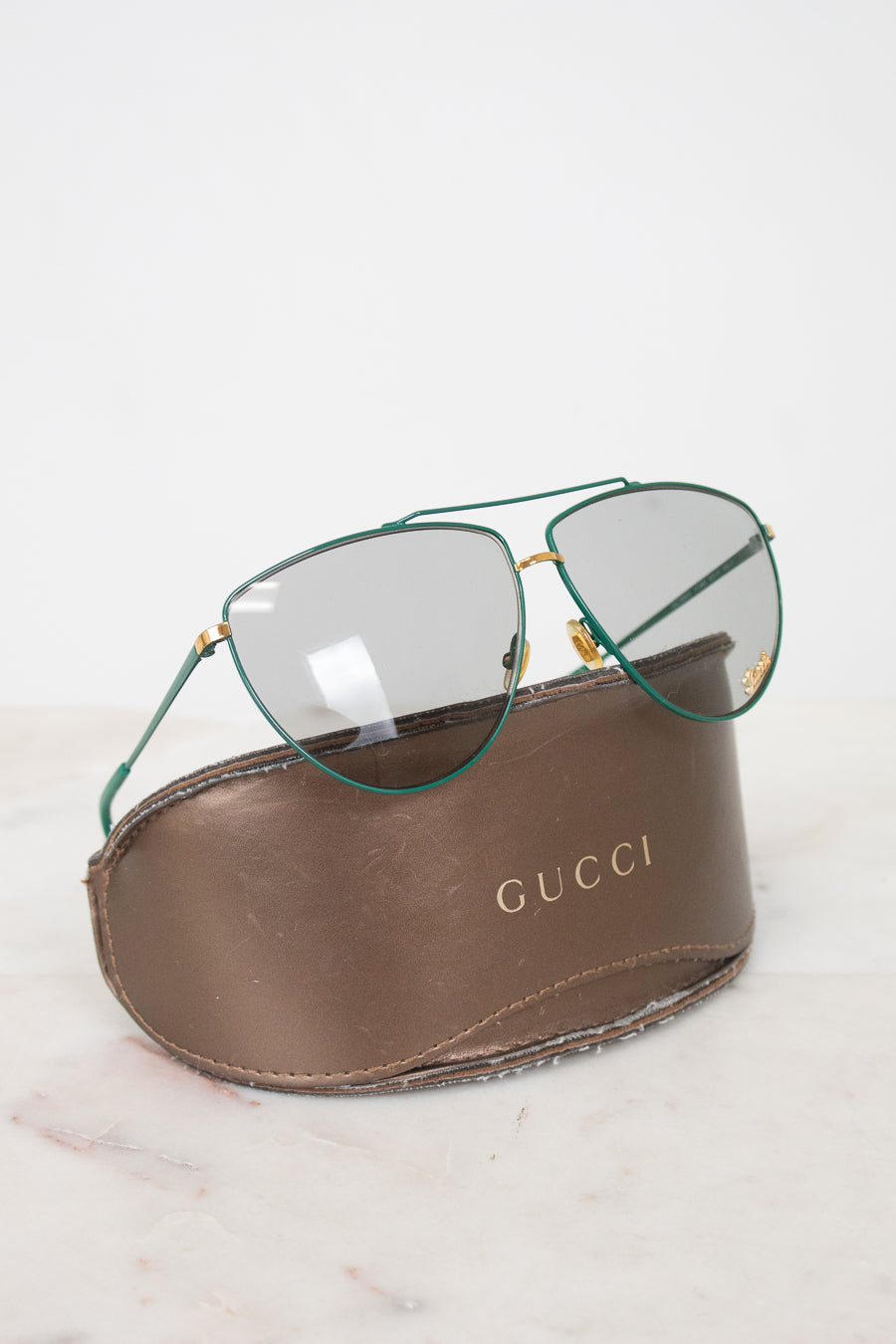 Teal aviator style glasses with gray lenses on a 'Gucci' case