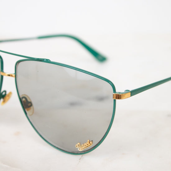 Close up of teal aviator frame with gold 'Gucci' brand detail on gray lens