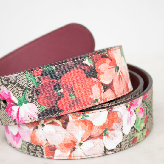 A rolled-up floral belt with a multicolor print of red, pink, and white flowers over a brown and beige patterned background, with a dark burgundy leather interior.