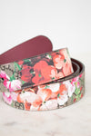 A rolled-up floral belt with a multicolor print of red, pink, and white flowers over a brown and beige patterned background, with a dark burgundy leather interior.