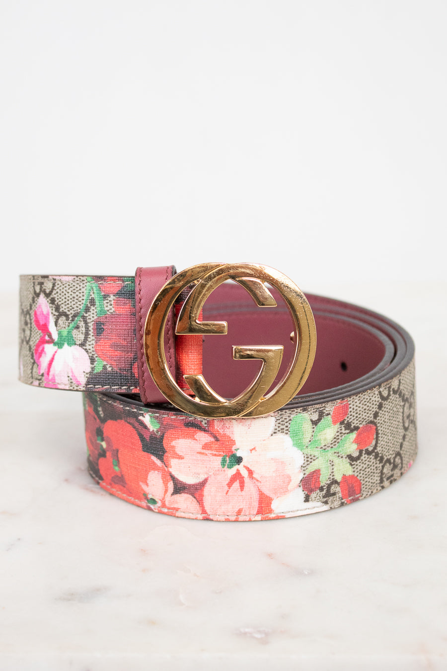A Gucci belt featuring a pink and red floral print over the brand's signature GG monogram canvas, finished with a polished gold-tone interlocking G buckle.