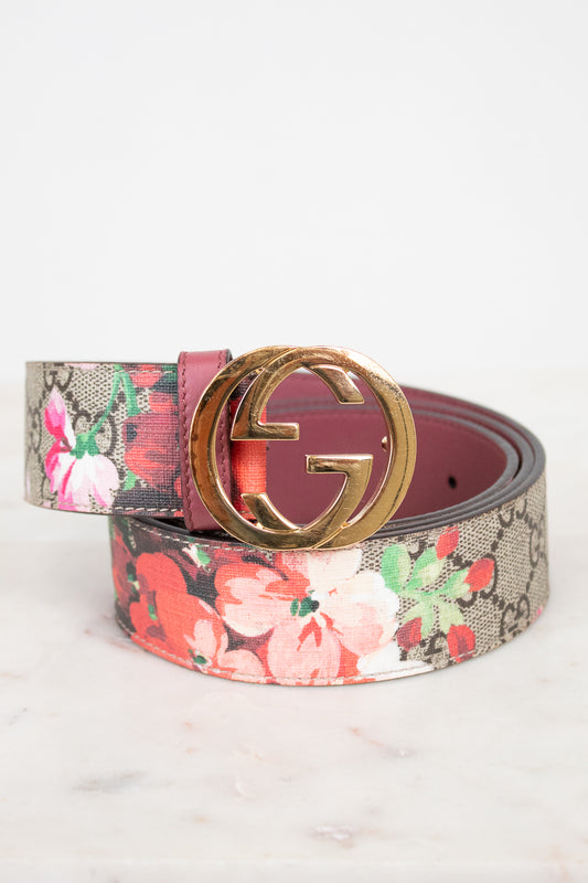 A Gucci belt featuring a pink and red floral print over the brand's signature GG monogram canvas, finished with a polished gold-tone interlocking G buckle.