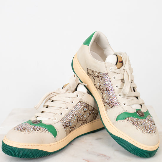A pair of low-top sneakers with beige panels, green accents on the heel and midsole, and a green outsole, displayed on a light marble surface against a white background.