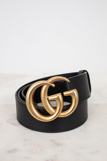 Black belt with gold double G buckle on a light marble background