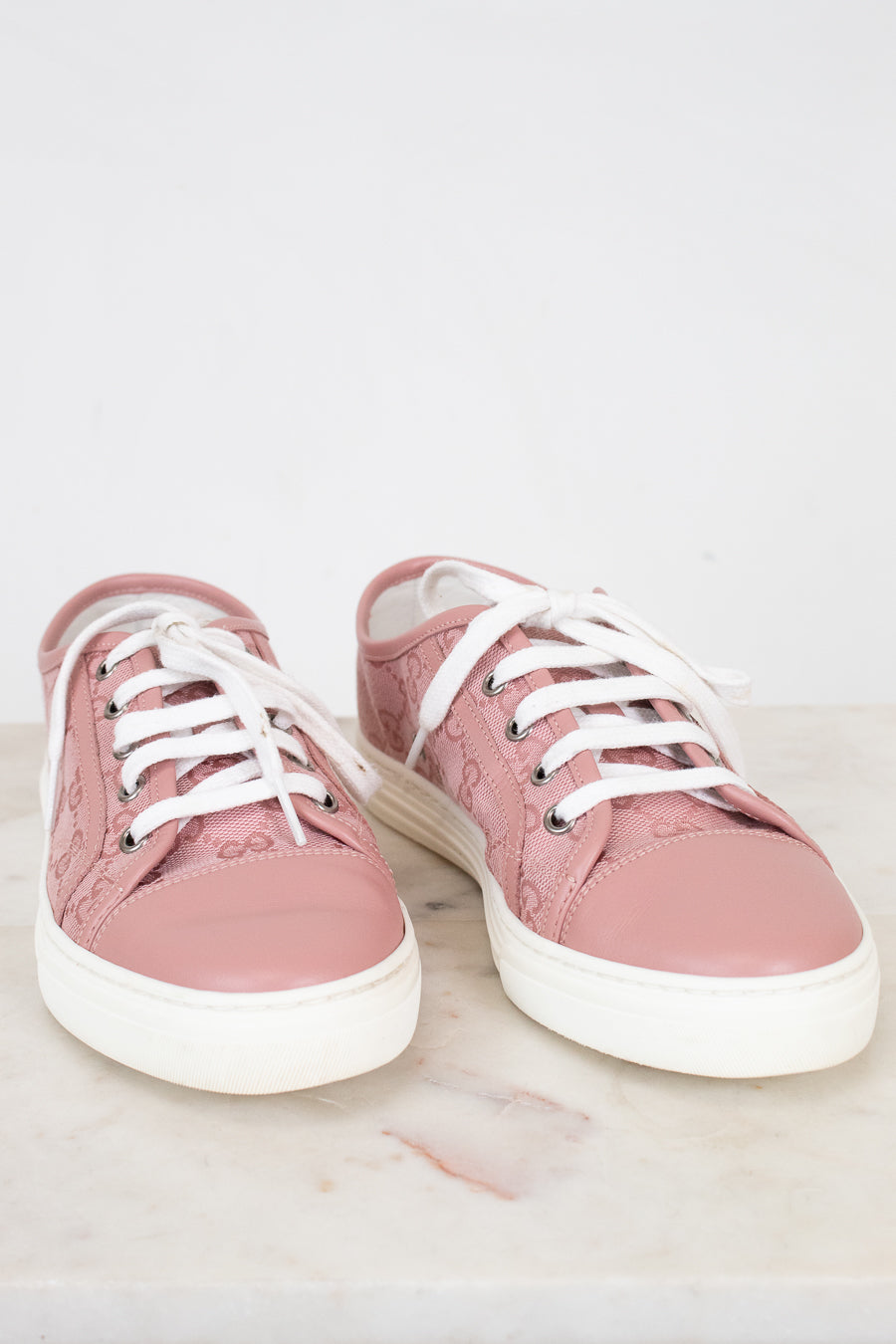 Pair of pink sneakers with white laces on a light background