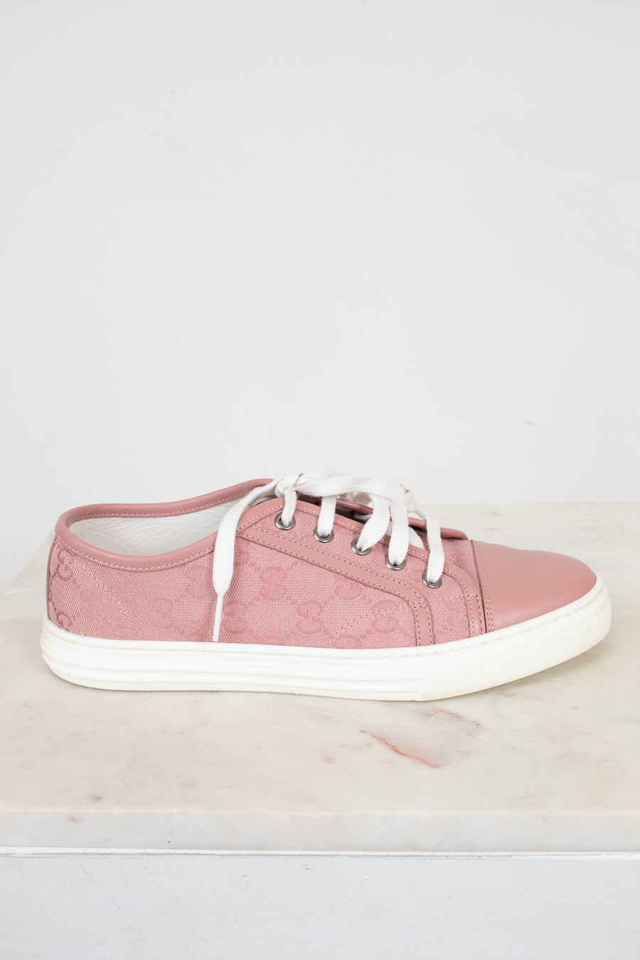 Pink sneaker with white laces on a light gray background