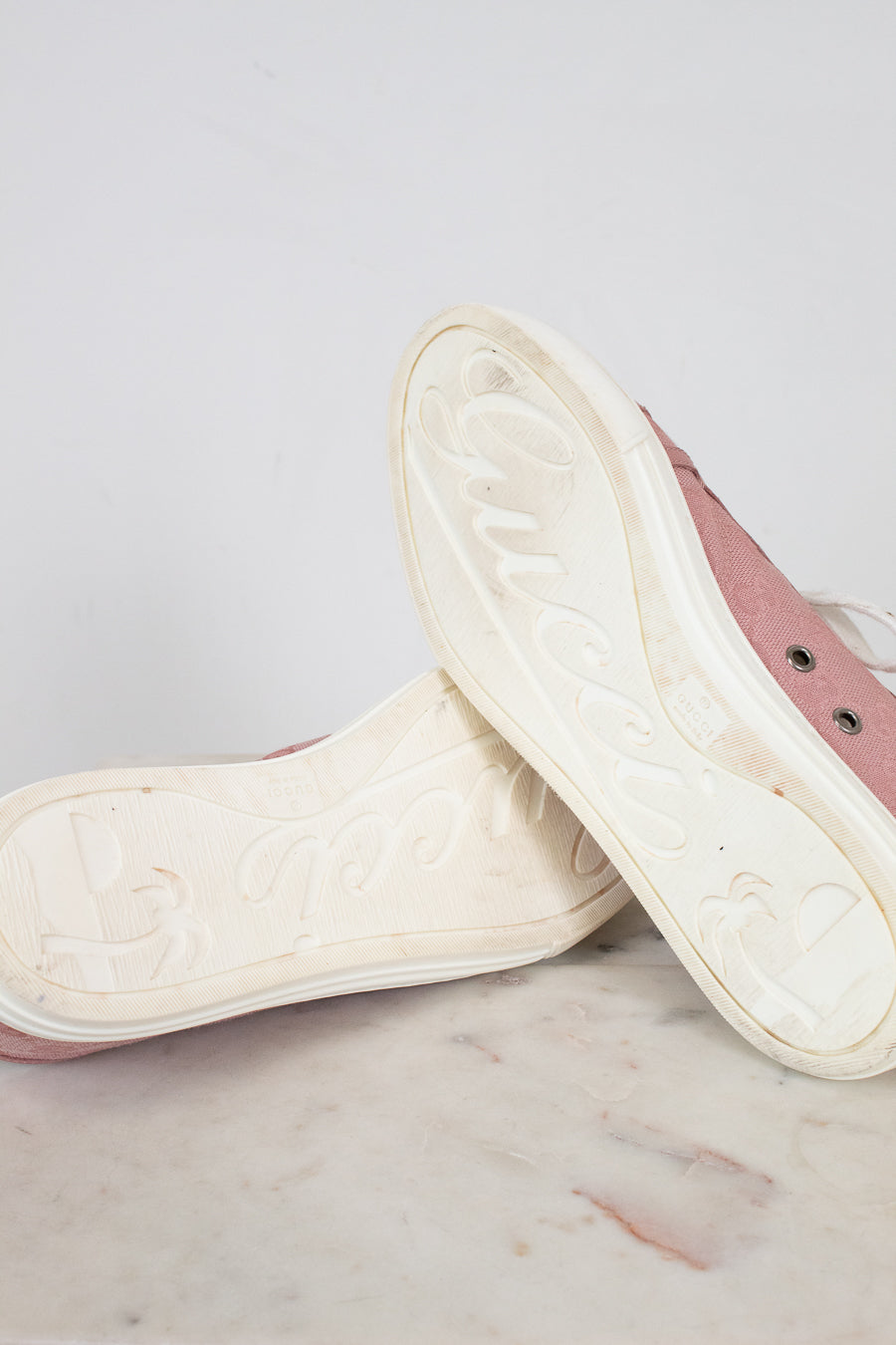 Close-up of white soles of pink sneakers on a marble surface with a light gray background