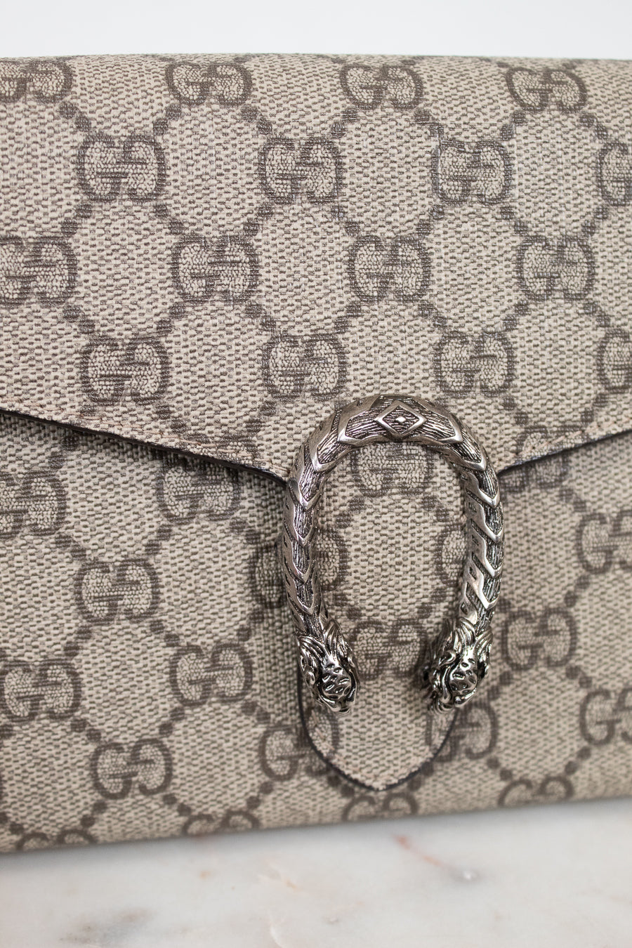 Close-up of a Gucci monogram coated canvas clutch bag with a silver-tone Dorothea buckle clasp on a light marble surface.
