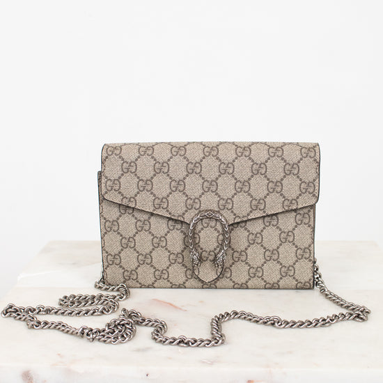 A beige and brown GG Supreme coated canvas shoulder bag with a silver-tone chain strap, displayed on a white marble surface against a white background.