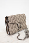 A Gucci shoulder bag in beige GG Supreme canvas with brown leather trim and a silver-tone chain strap, displayed on a light marble surface against a white background.