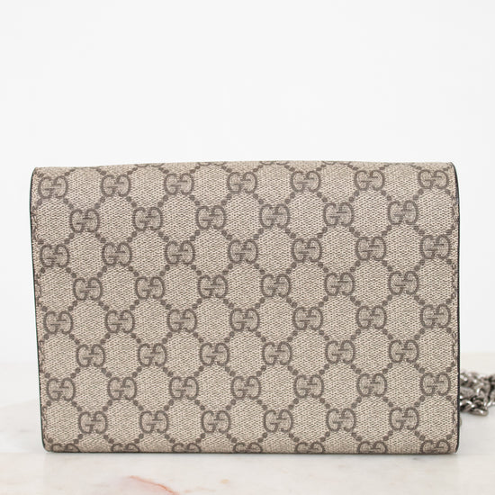 A Gucci monogram canvas chain bag in beige and brown, resting on a light marble surface against a white background.