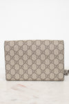 A Gucci monogram canvas chain bag in beige and brown, resting on a light marble surface against a white background.