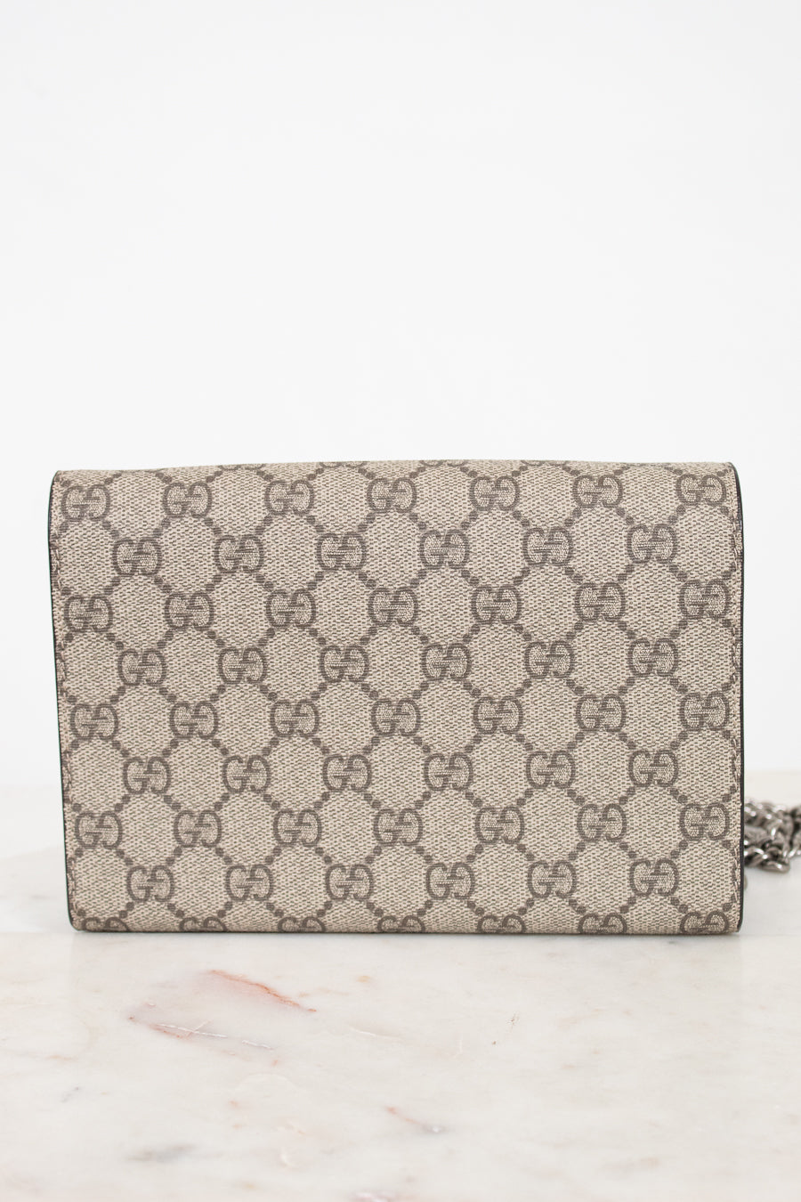 A Gucci monogram canvas chain bag in beige and brown, resting on a light marble surface against a white background.