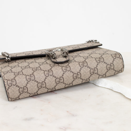 A Gucci monogram canvas clutch bag with a silver-tone horsebit clasp, resting on a white marble surface against a white background.