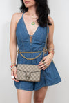 A woman wearing a blue denim romper and holding a beige Gucci GG Supreme shoulder bag with a silver-tone chain strap, against a plain light gray background.