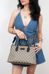 A woman wearing a denim romper carries a beige and brown GG Supreme monogram handbag with black leather handles.
