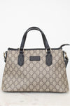 A beige and brown monogram handbag with black leather handles and trim, featuring the interlocking GG pattern and a central logo plaque.