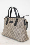 A beige and brown GG Supreme canvas handbag with black leather handles and trim, shown on a light marble surface against a white background.