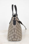A small Gucci handbag in beige and brown GG Supreme canvas with black leather handles and trim, shown from the side on a light marble surface against a white background.
