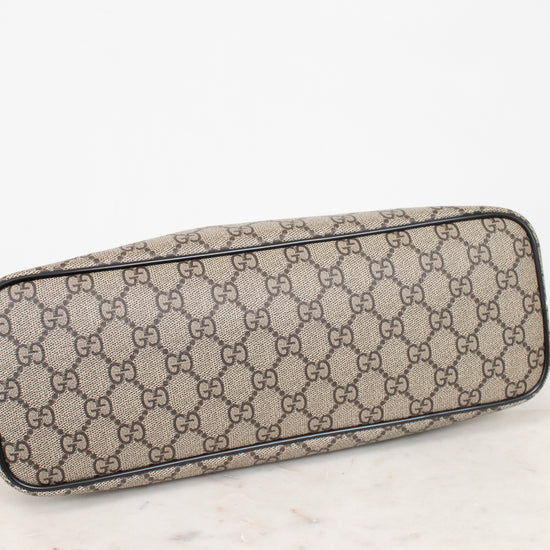 A Gucci monogram canvas bottom view or small bag with a beige and brown GG pattern, resting on a white marble surface against a white background.