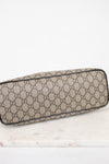 A Gucci monogram canvas bottom view or small bag with a beige and brown GG pattern, resting on a white marble surface against a white background.