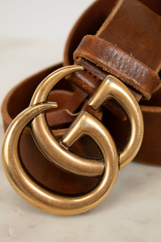Brown leather belt with a gold buckle on a light background