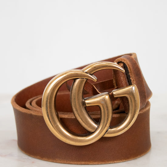 Brown leather belt with gold double G buckle on a light background