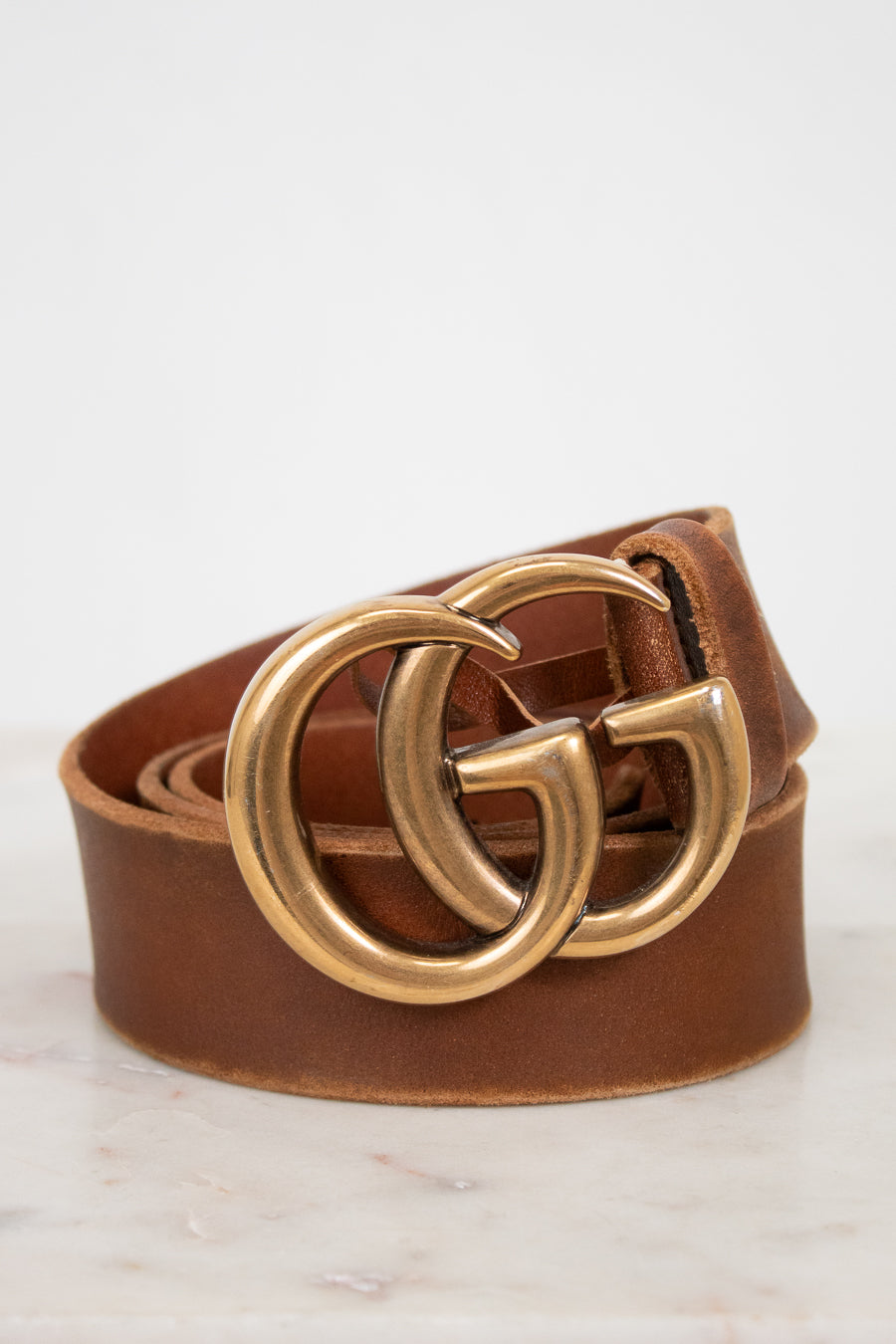 Brown leather belt with gold double G buckle on a light background