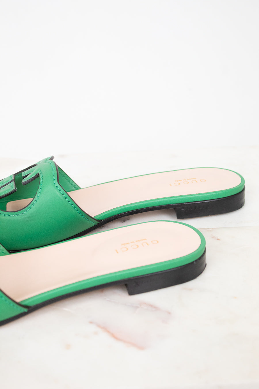 Side back view of green leather GG slides showing black heel detail and displayed against a marble surface