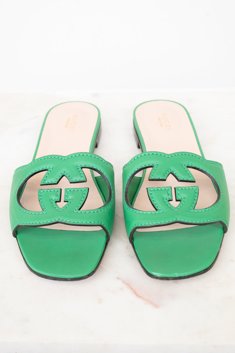 Green leather GG slides shown against a marble surface