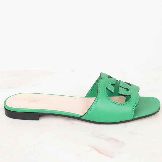 Side view of green leather GG slides shown against a marble surface
