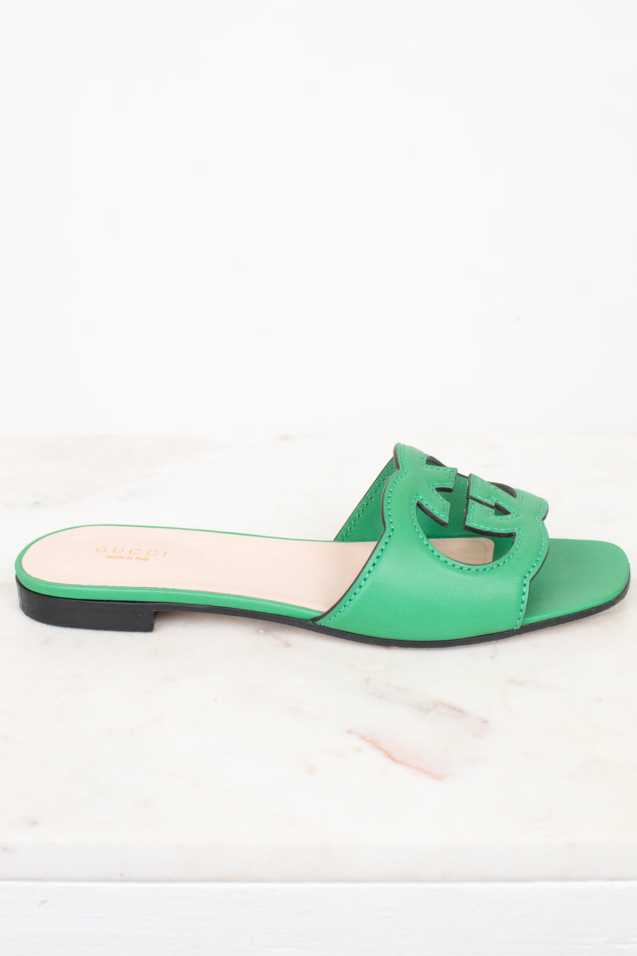 Side view of green leather GG slides shown against a marble surface