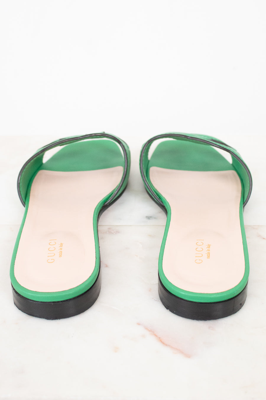 Heel view of green leather GG slides showing black heel detail and displayed against a marble surface